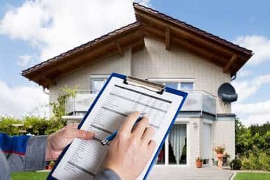 A home inspector holding a clipboard with a checklist in front of a modern suburban house.
